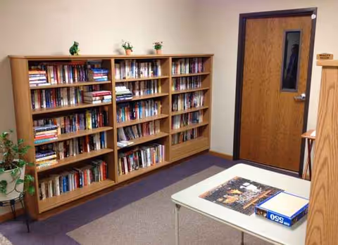 Quiet reading area in a senior living facility with tall wood bookshelves and a table.
