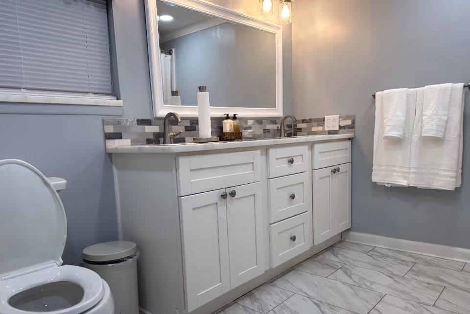 A modern gray and white bathroom with a double-sink vanity, large mirror, toilet, and towel rack.