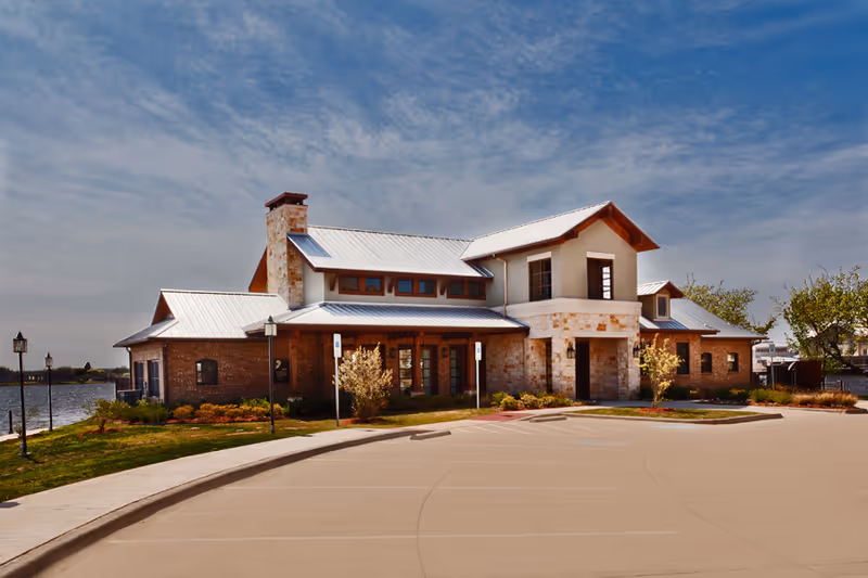 Front exterior of a two-story waterfront building with stone and brick facade and a metal roof under a blue sky.