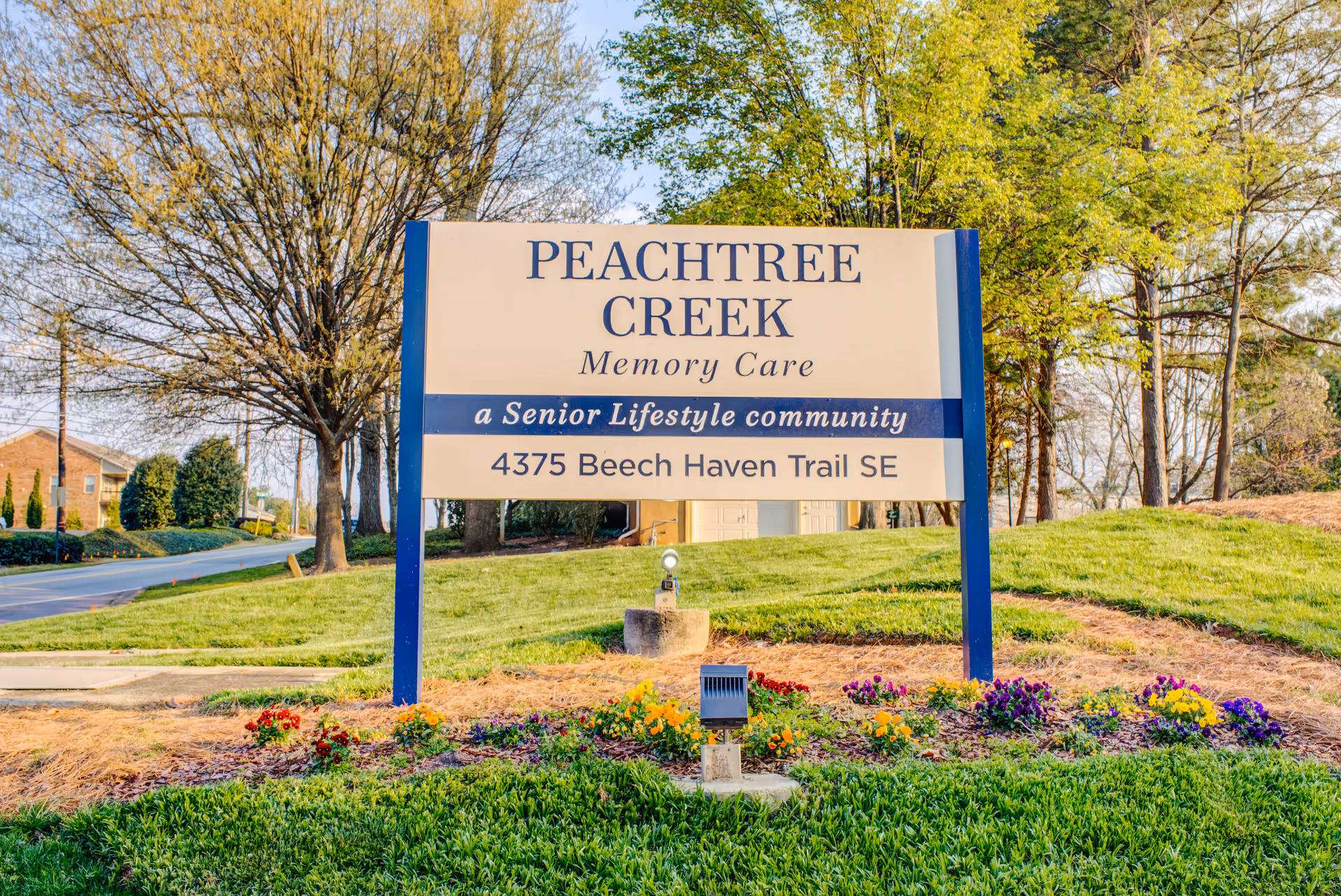 Outdoor sign for Peachtree Creek Memory Care, a senior lifestyle community, located at 4375 Beech Haven Trail SE, surrounded by grass, flowers, and trees.
