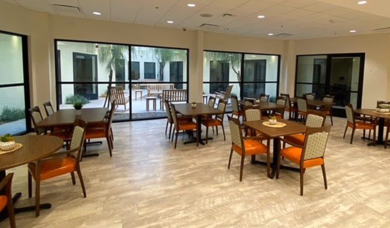 Spacious dining room with multiple tables and chairs and large windows looking out to an enclosed courtyard.