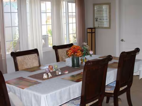 A dining room with a long table, chairs, flowers centerpiece, and windows.