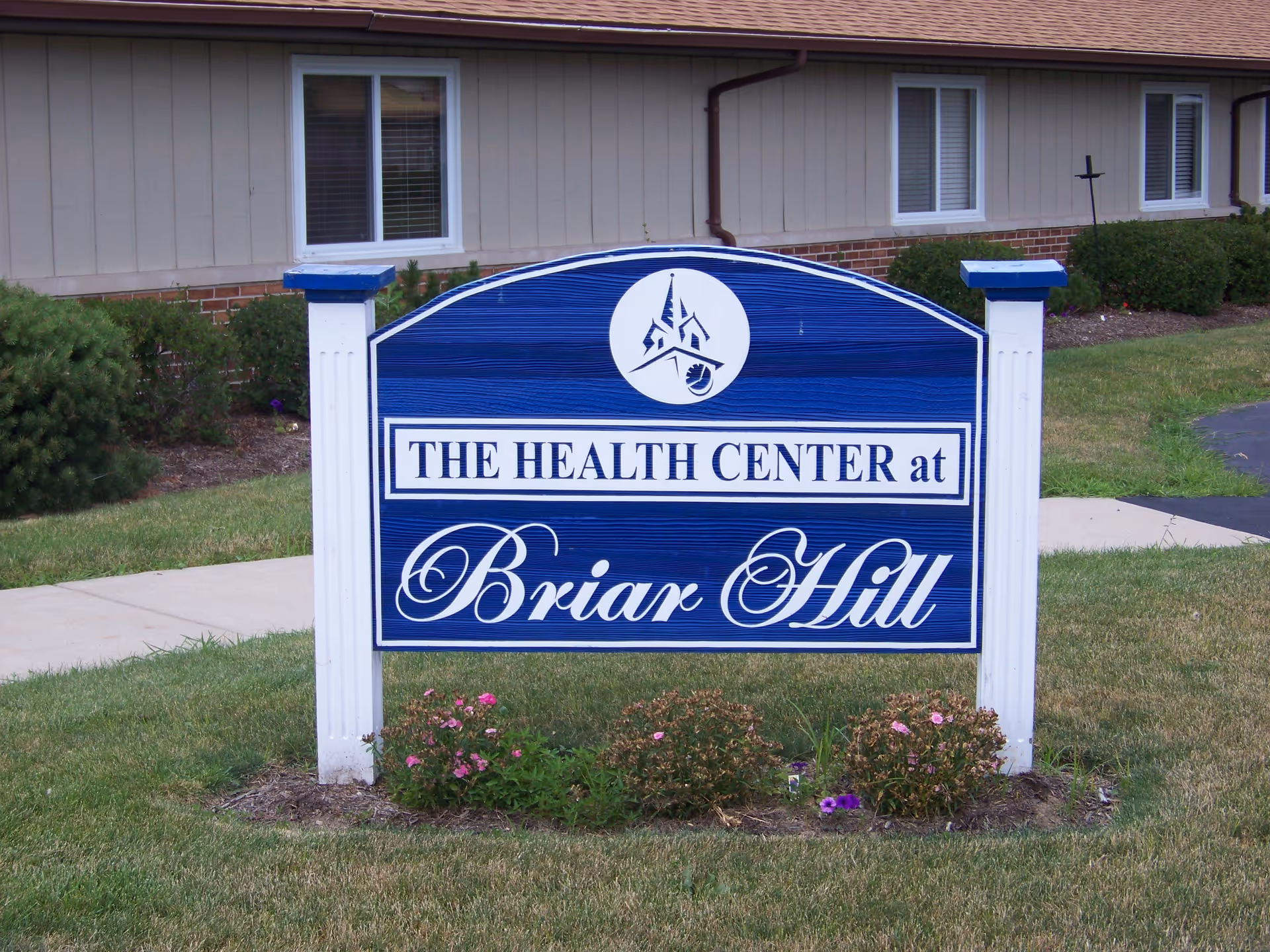 Blue sign reading "The Health Center at Briar Hill" on a lawn in front of a single-story building.