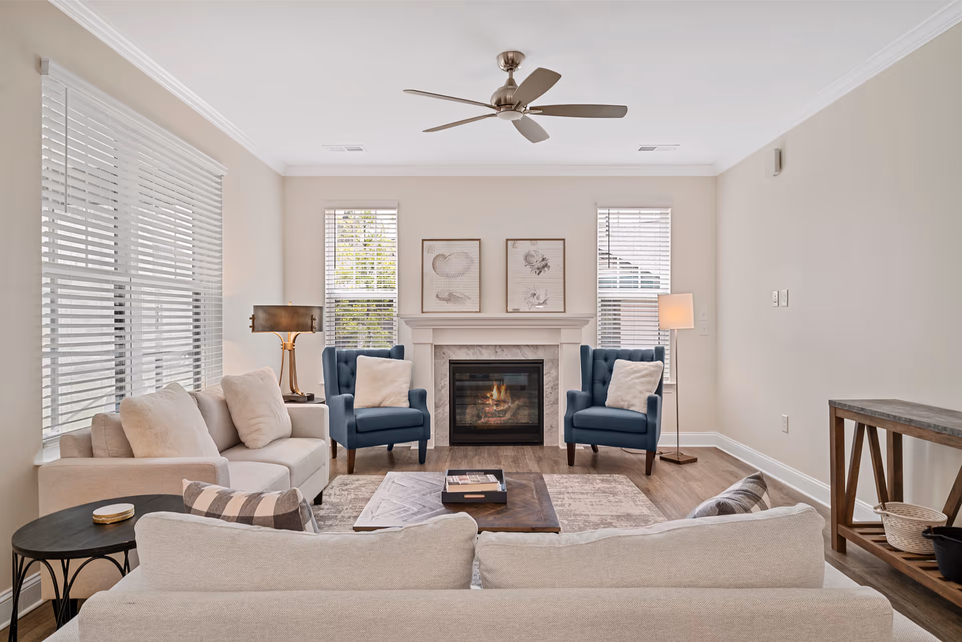 Bright living room with neutral sofas, two blue armchairs, a fireplace, and a ceiling fan.