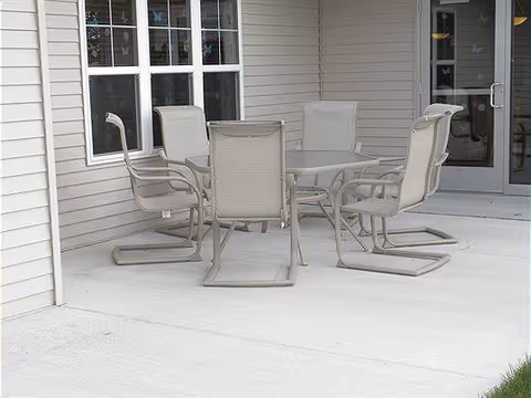 Outdoor patio with a round table and six beige chairs beside a building.