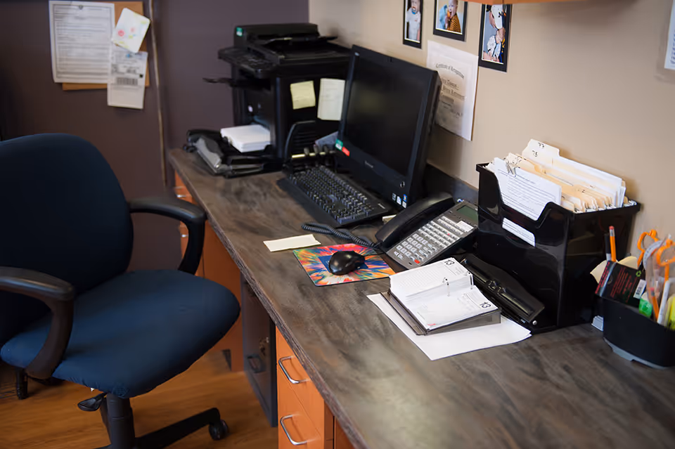 Office/reception desk with a computer, phone, file organizers, and a blue swivel chair.