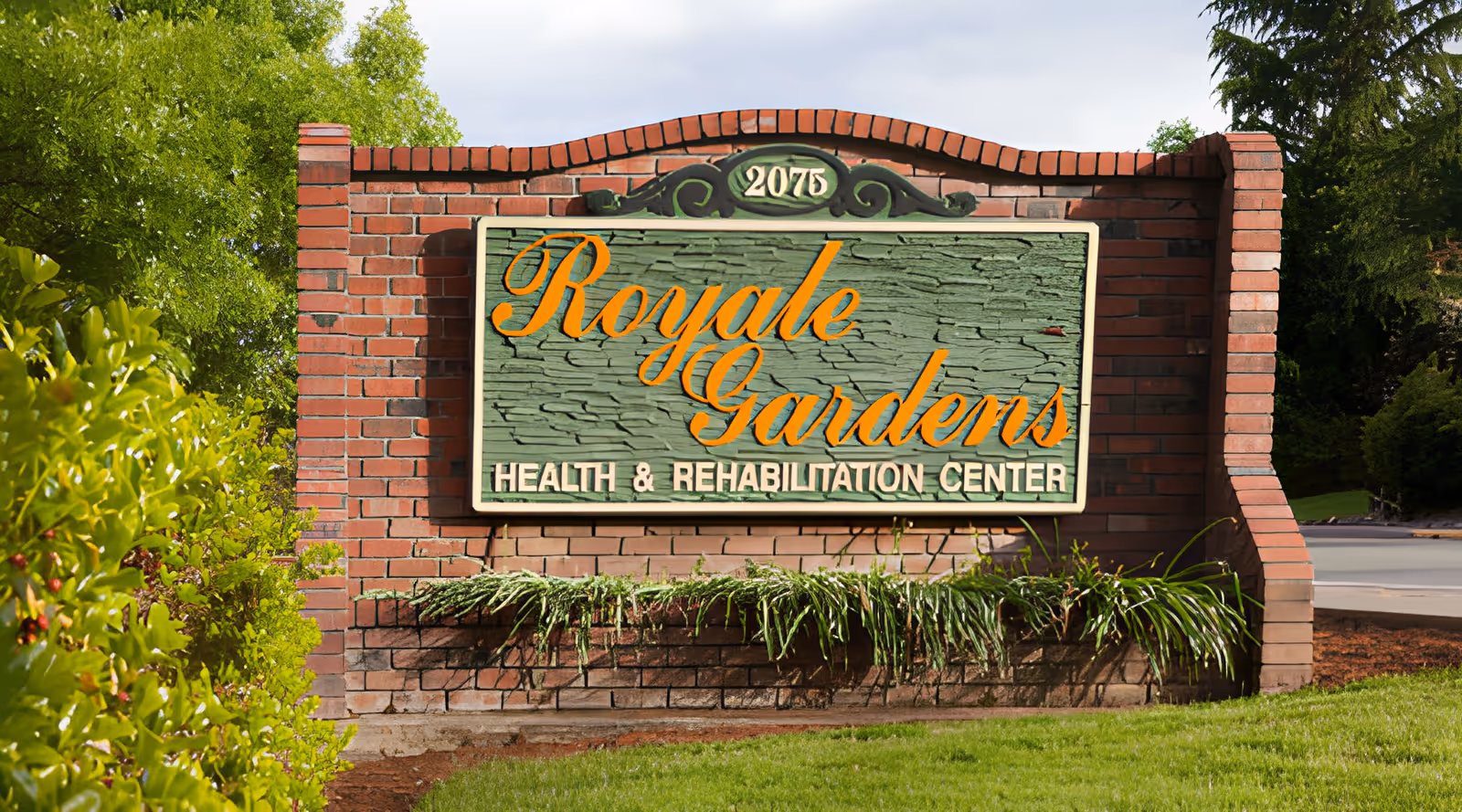 Brick entrance sign reading 'Royale Gardens Health & Rehabilitation Center' surrounded by landscaping.