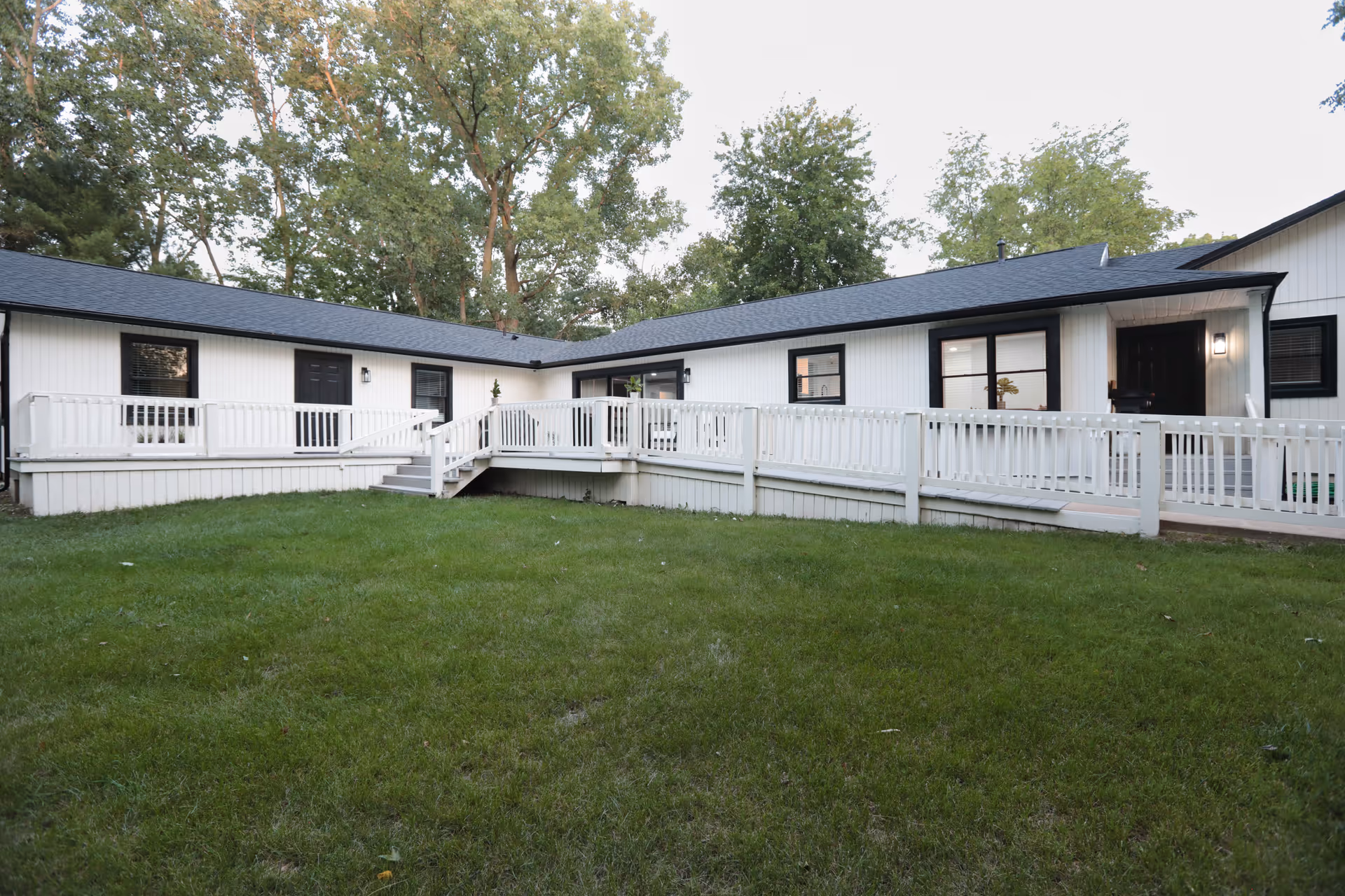 Single-story white senior living building with black trim, a wraparound ramp and a grassy yard in front.