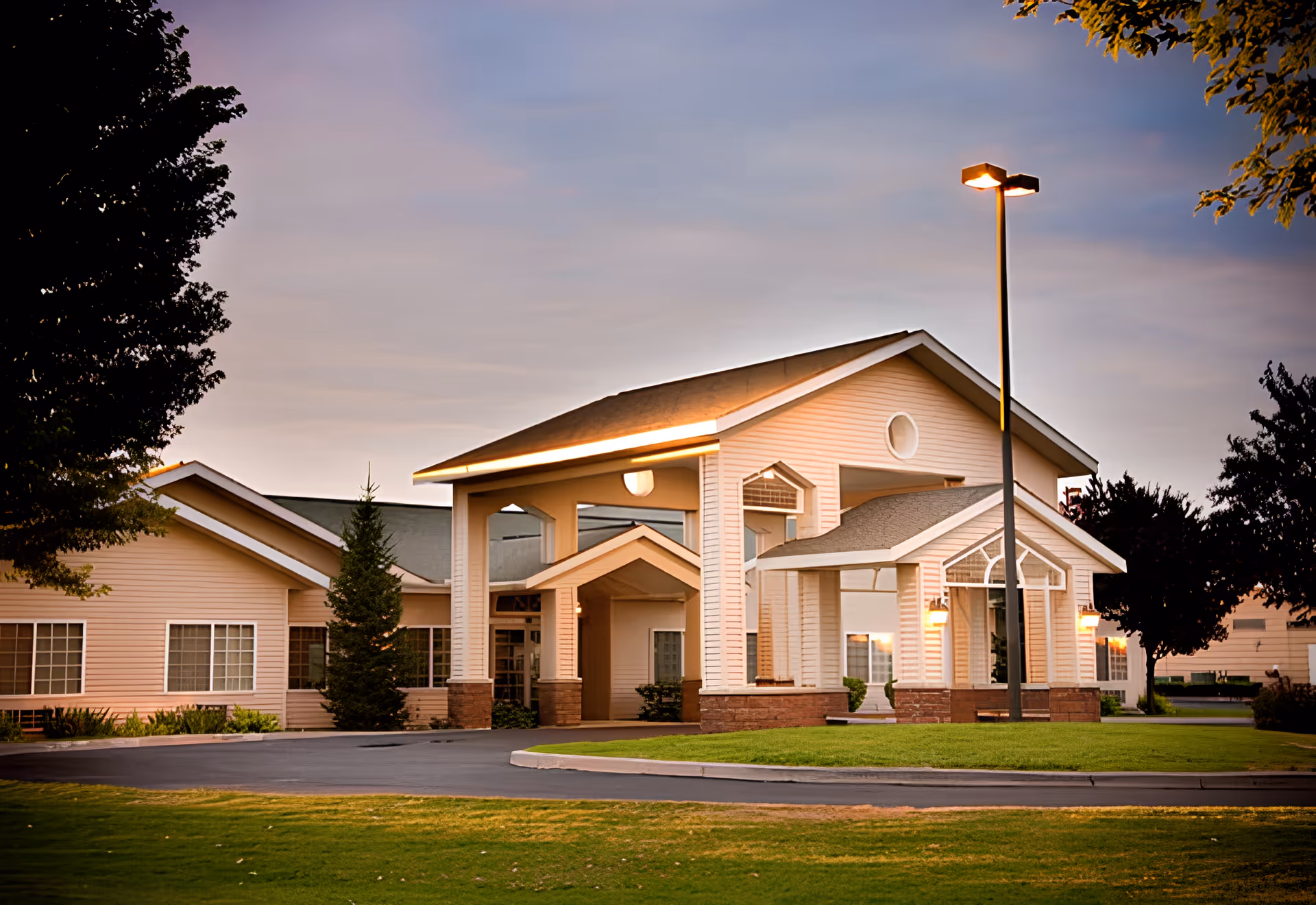 Exterior view of Cheney Care Center building during dusk with warm lighting, a covered entrance, surrounding trees, and a well-maintained lawn.