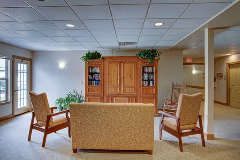 A comfortable common lounge with a sofa and three chairs facing a wooden cabinet/bookcase in a well-lit interior space.