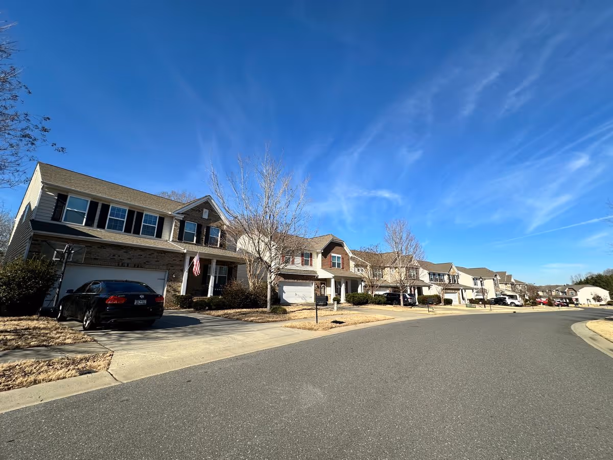 Row of two-story suburban houses with driveways and parked cars under a clear blue sky.