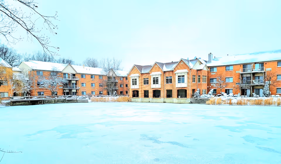 Snow-covered Mallard Cove senior living buildings facing a frozen pond.