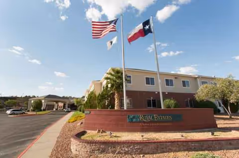 Front exterior of Royal Estates of El Paso with flags, sign, and landscaped entry.