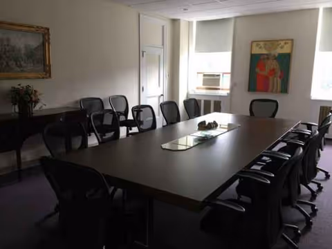 A conference room with a long table surrounded by office chairs in a senior facility.