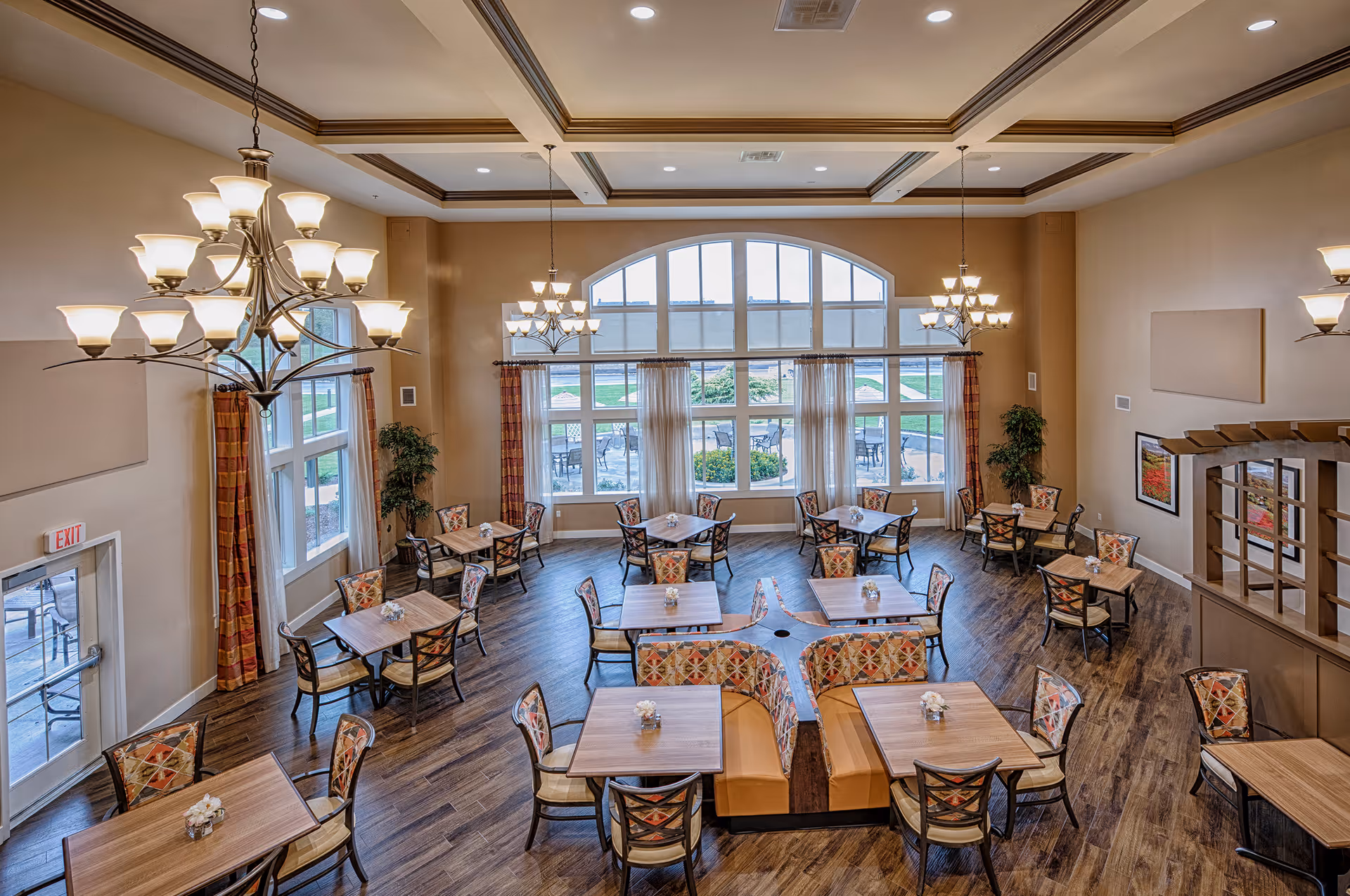 Spacious dining room with multiple tables and chairs, patterned seating, large arched windows, and chandeliers.