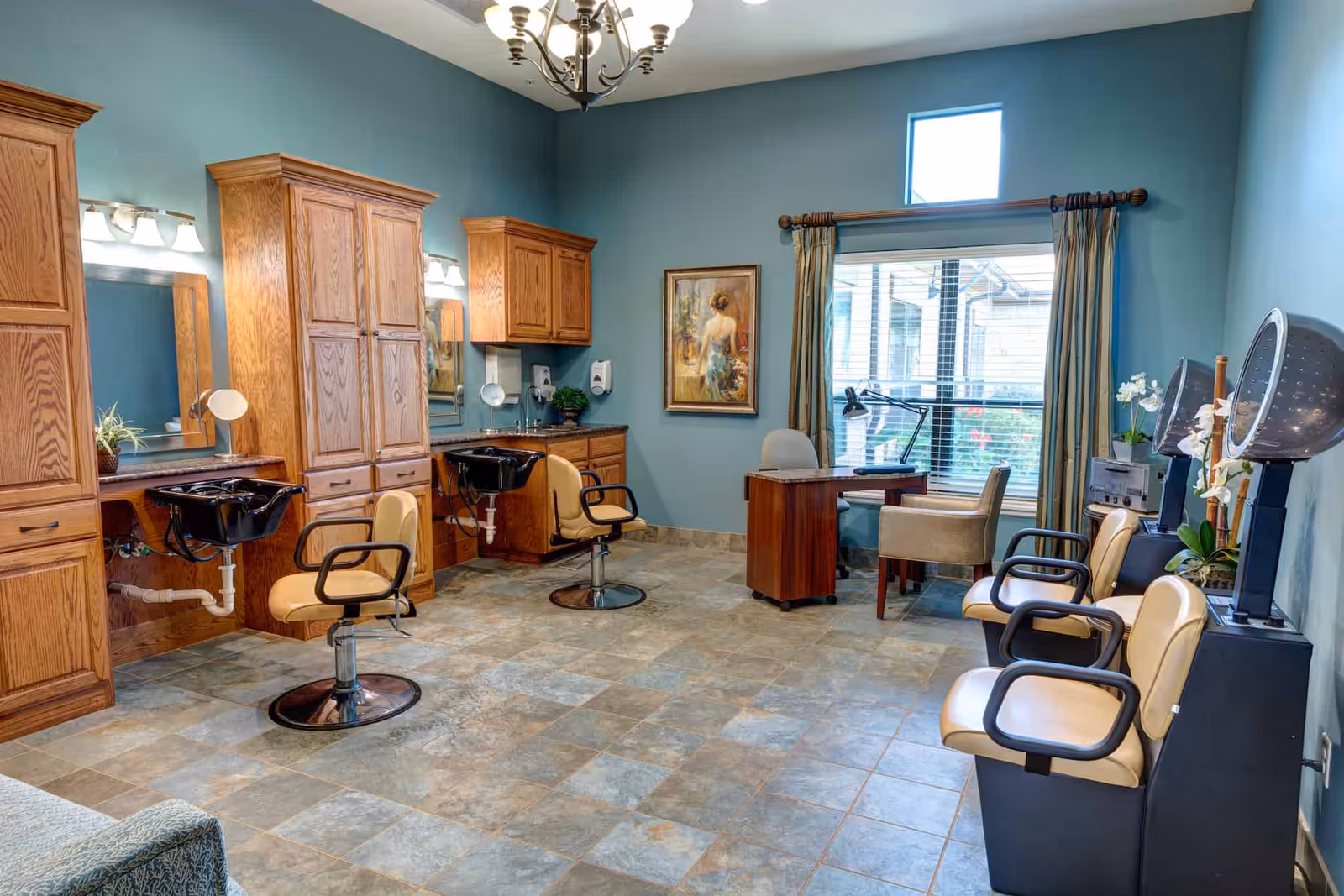 Salon room with styling chairs, shampoo sinks, hooded hair dryers, wooden cabinets, and a desk by a window.