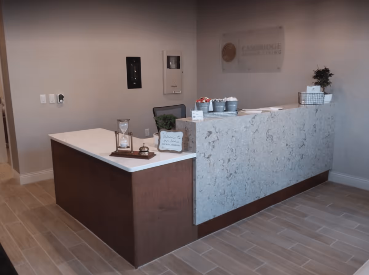 Reception desk inside the Cambridge Senior Living lobby with a marble-front counter, decorative items, and a wall sign.