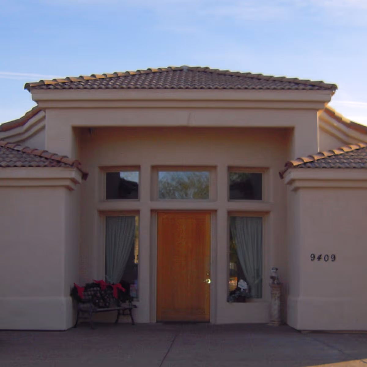 Front entrance of a stucco building with a wooden door, tall windows, tile roof, and the address number 9409.