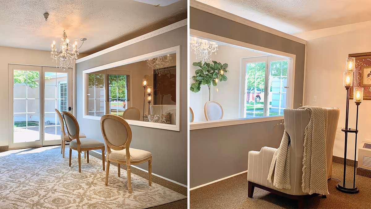 Bright seating area with an upholstered armchair, three wooden chairs on a patterned rug, a chandelier, and a large interior window.