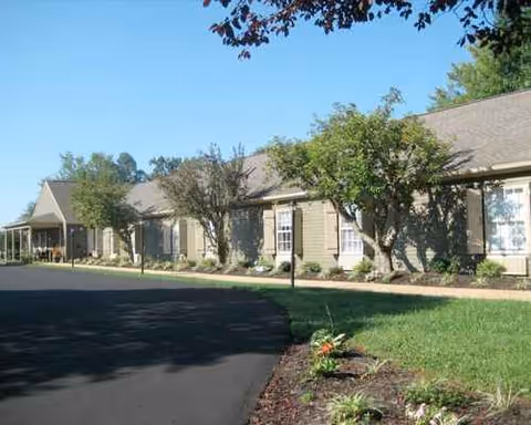 Exterior view of a single-story senior living building with trees and a parking lot.