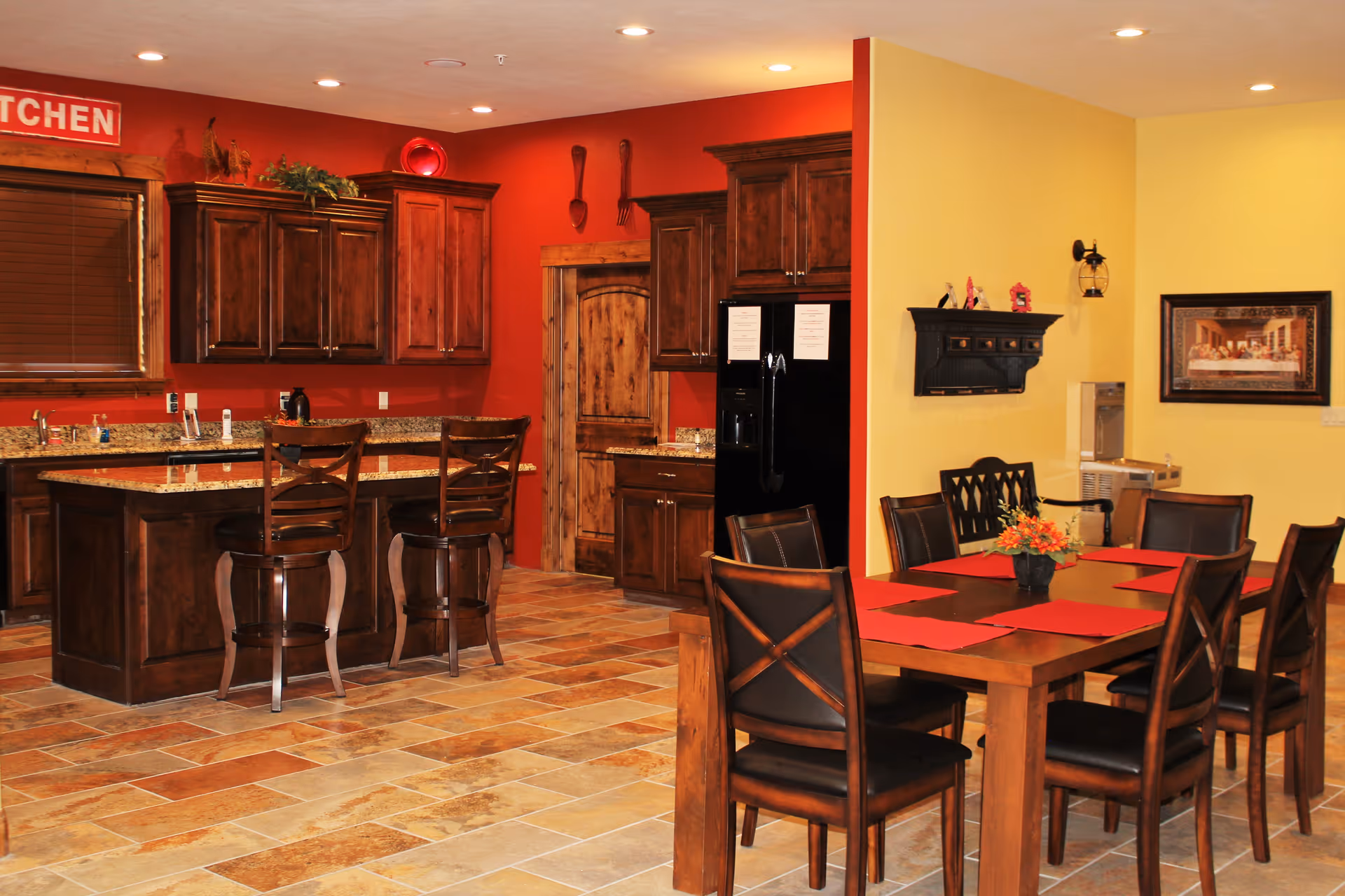 Open communal kitchen and dining area with a granite island, dark wooden cabinets, and a dining table with chairs.