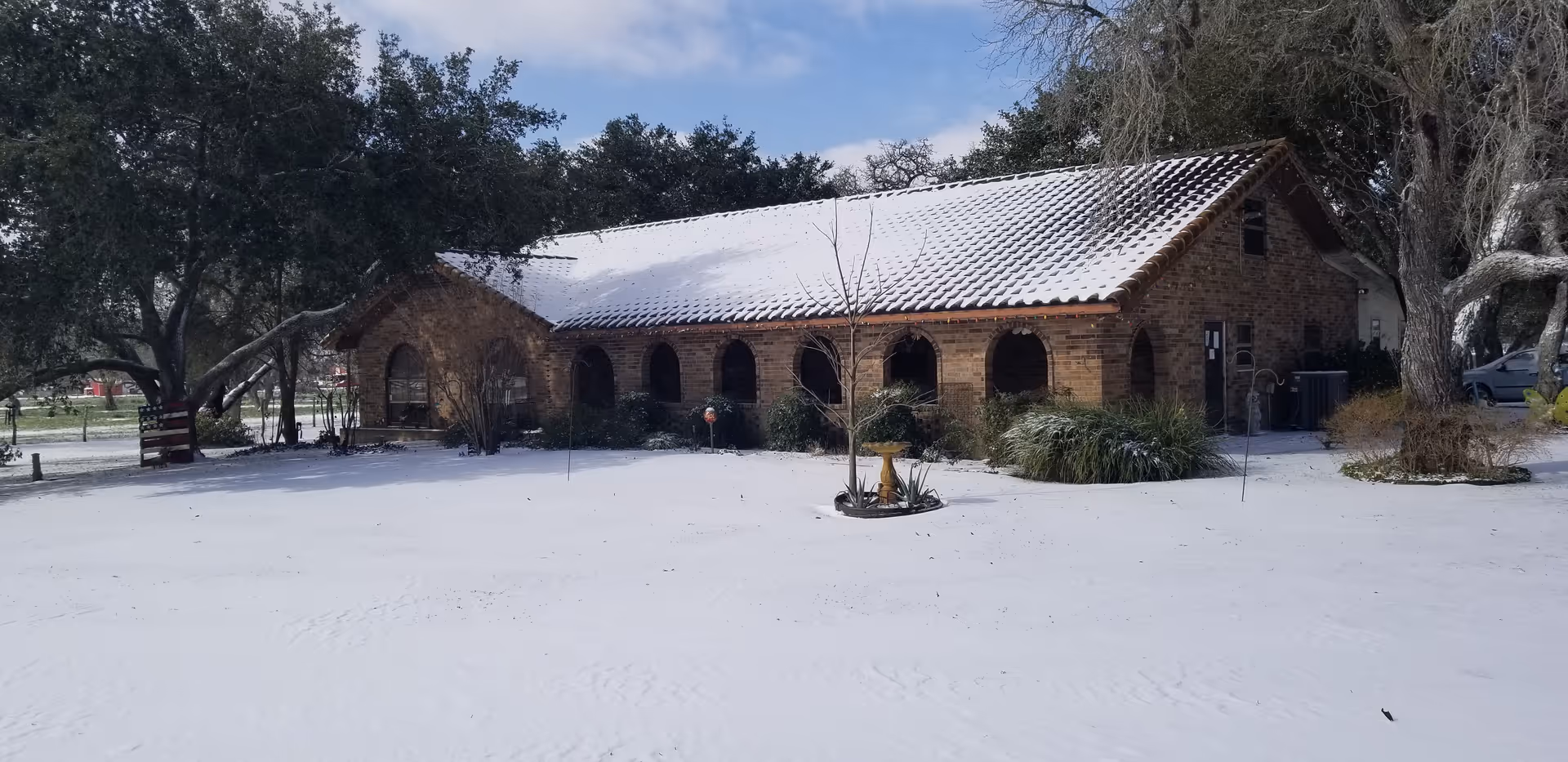 One-story brick building with arched veranda and snow-covered roof and yard surrounded by trees.