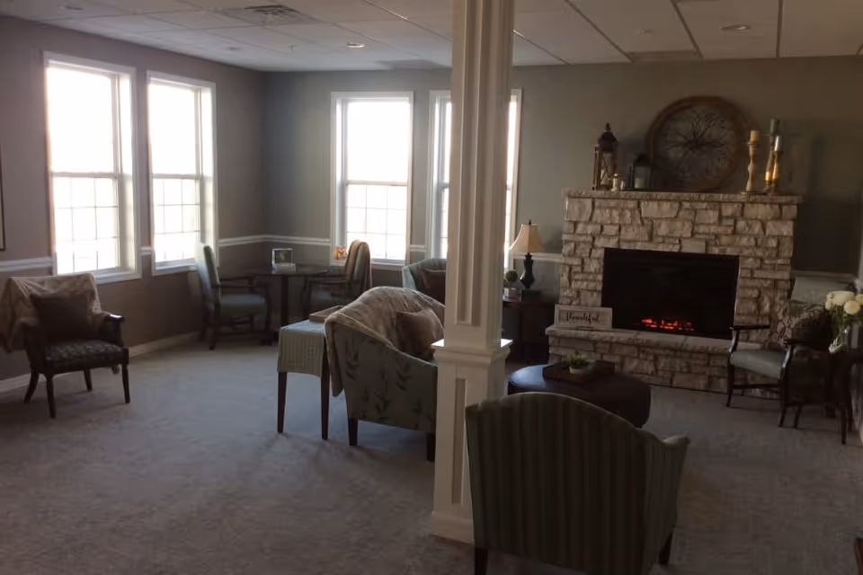 Bright seating lounge with armchairs, a central column, and a stone fireplace.