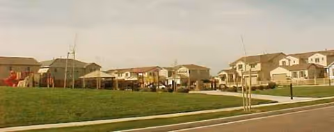 Exterior view of a senior living campus with beige houses, green lawn, and sidewalks.