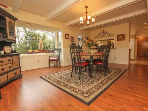 A cozy dining room with a round wooden table, chairs, rug, and window view.