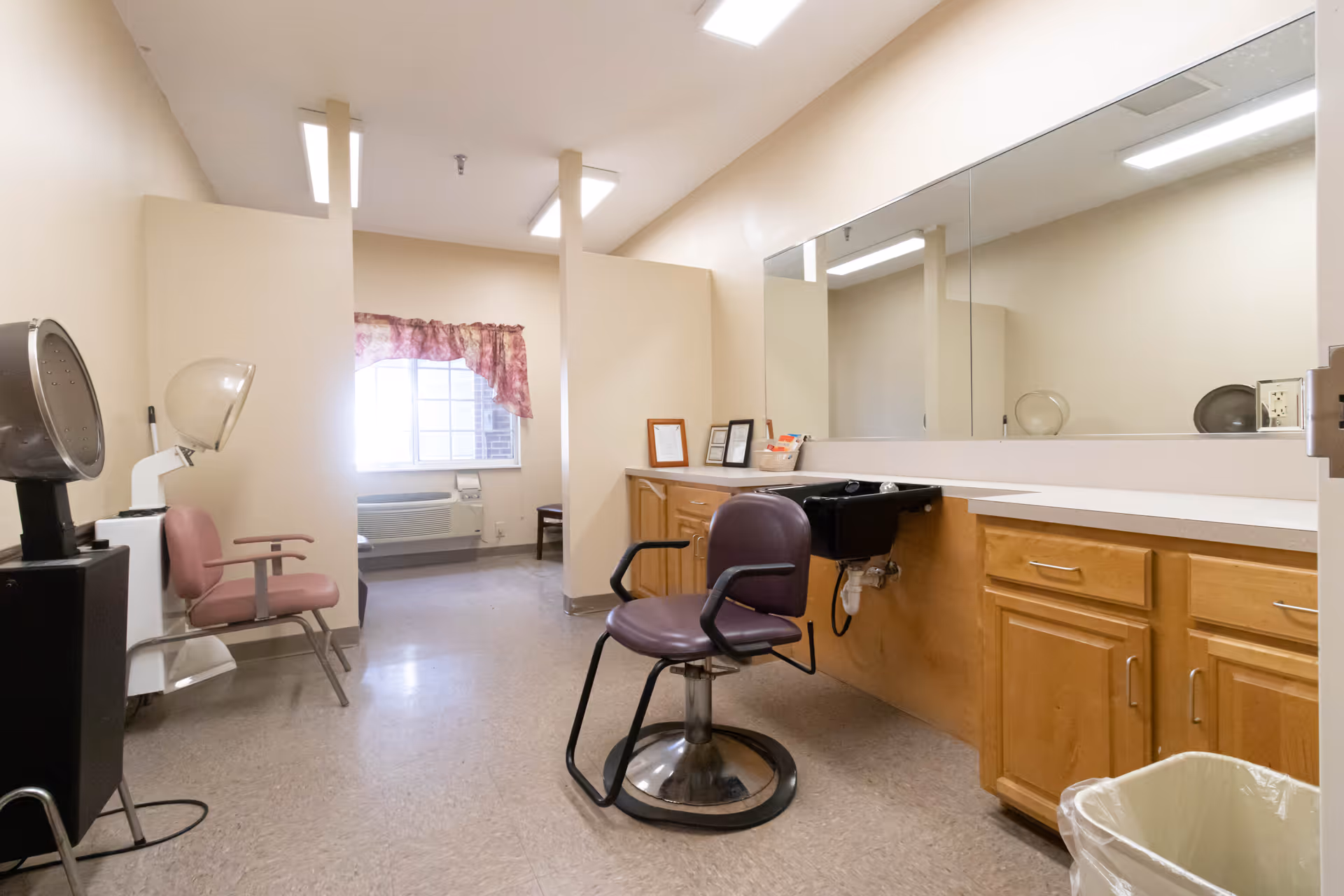 Interior salon/hair-styling room with a chair, hooded dryer, wash sink, large mirror and cabinetry.