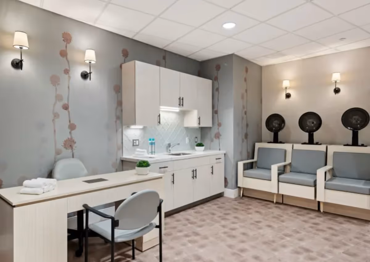 Salon-style interior with a manicure table and chairs, white cabinets, and three hooded hair-dryer stations.