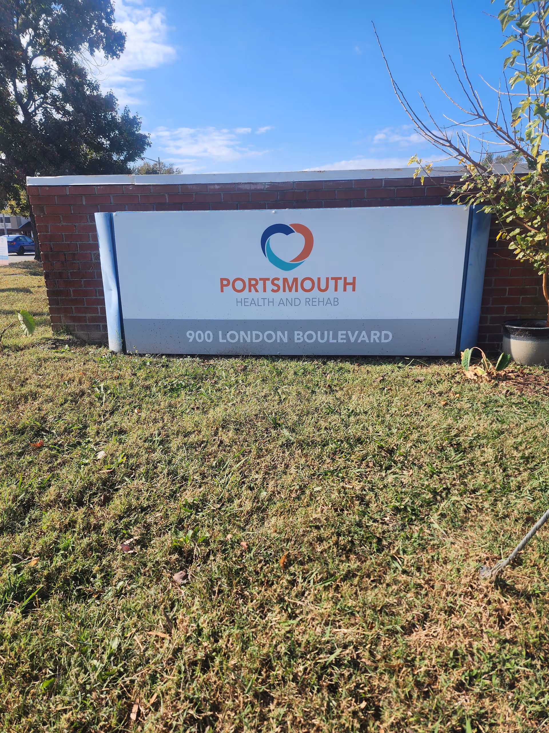 Outdoor sign for Portsmouth Health and Rehab with logo and address '900 London Boulevard' in front of a brick wall and grassy lawn.