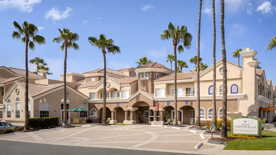 Front exterior of Atria Newport Plaza senior living building with palm trees and a circular driveway.