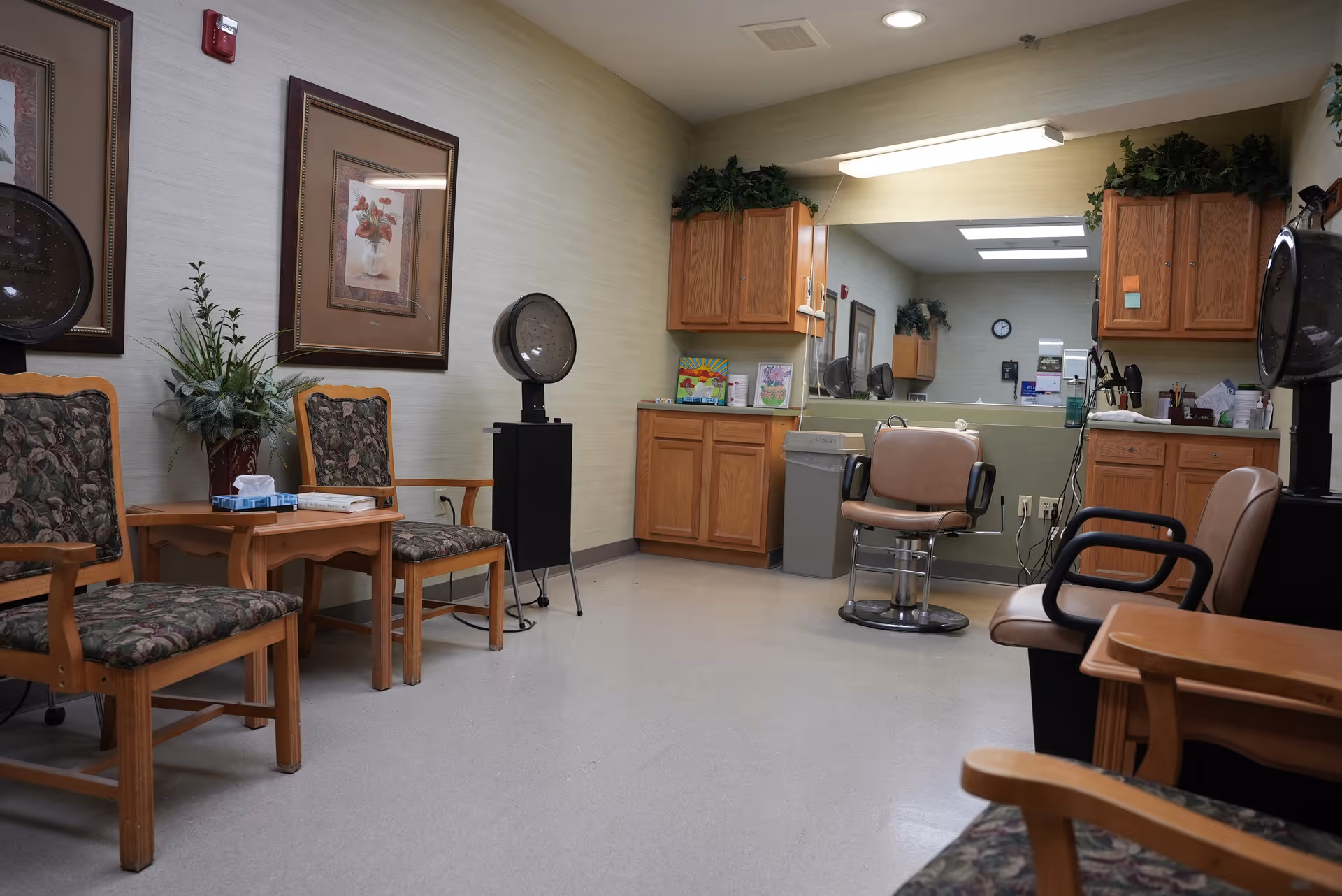 A small salon-style room with styling chairs, hooded hair dryers, waiting chairs, cabinets and a large mirror.