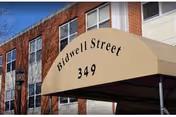 Exterior view of a brick building with multiple windows and a beige awning above the entrance displaying the text 'Bidwell Street 349'.