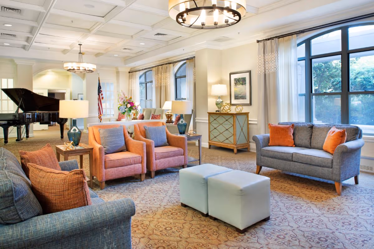 Spacious, well-lit lounge with sofas, armchairs, ottomans, a grand piano, and large windows.