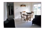 Interior view of a dining area with a wooden table and four chairs between a living room and a sliding glass door.