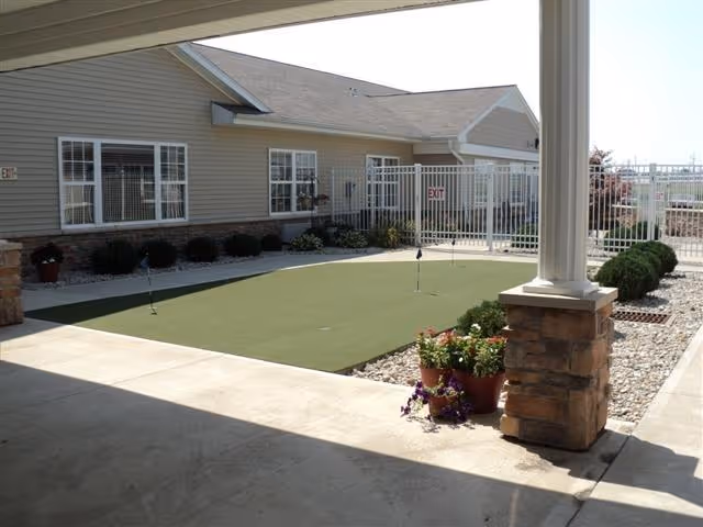 Covered courtyard with a small putting green, potted flowers, and the exterior of the senior living building.