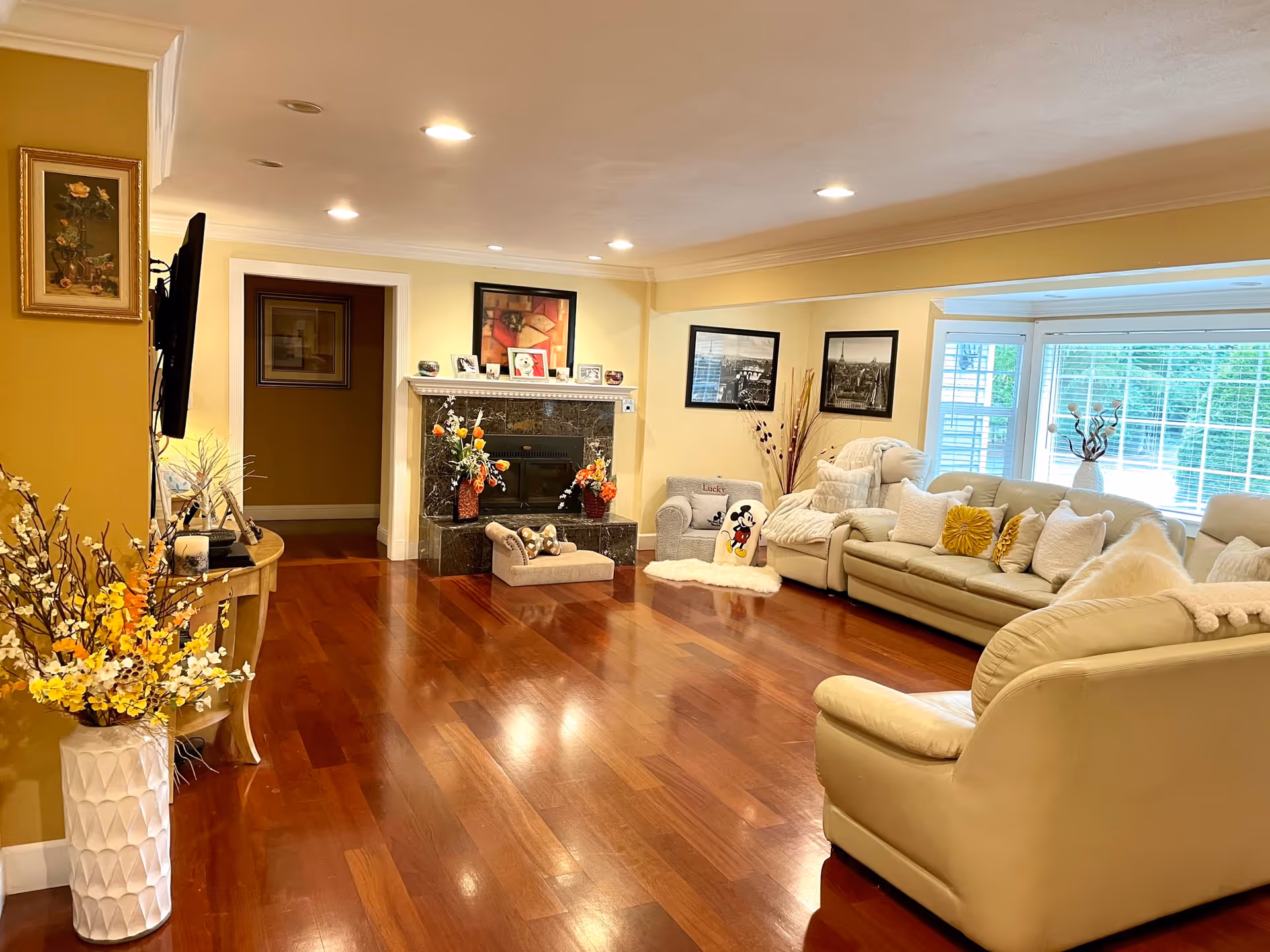 Spacious, well-lit living room with cream leather sofas, hardwood floors, a fireplace, and large windows.