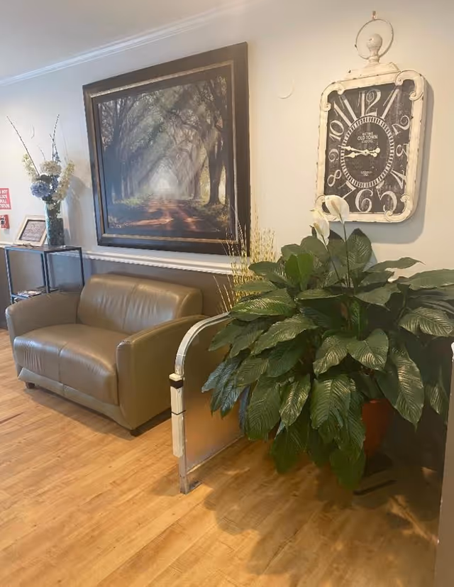 A cozy seating area with a sofa, potted plant, wall art, and a decorative clock.