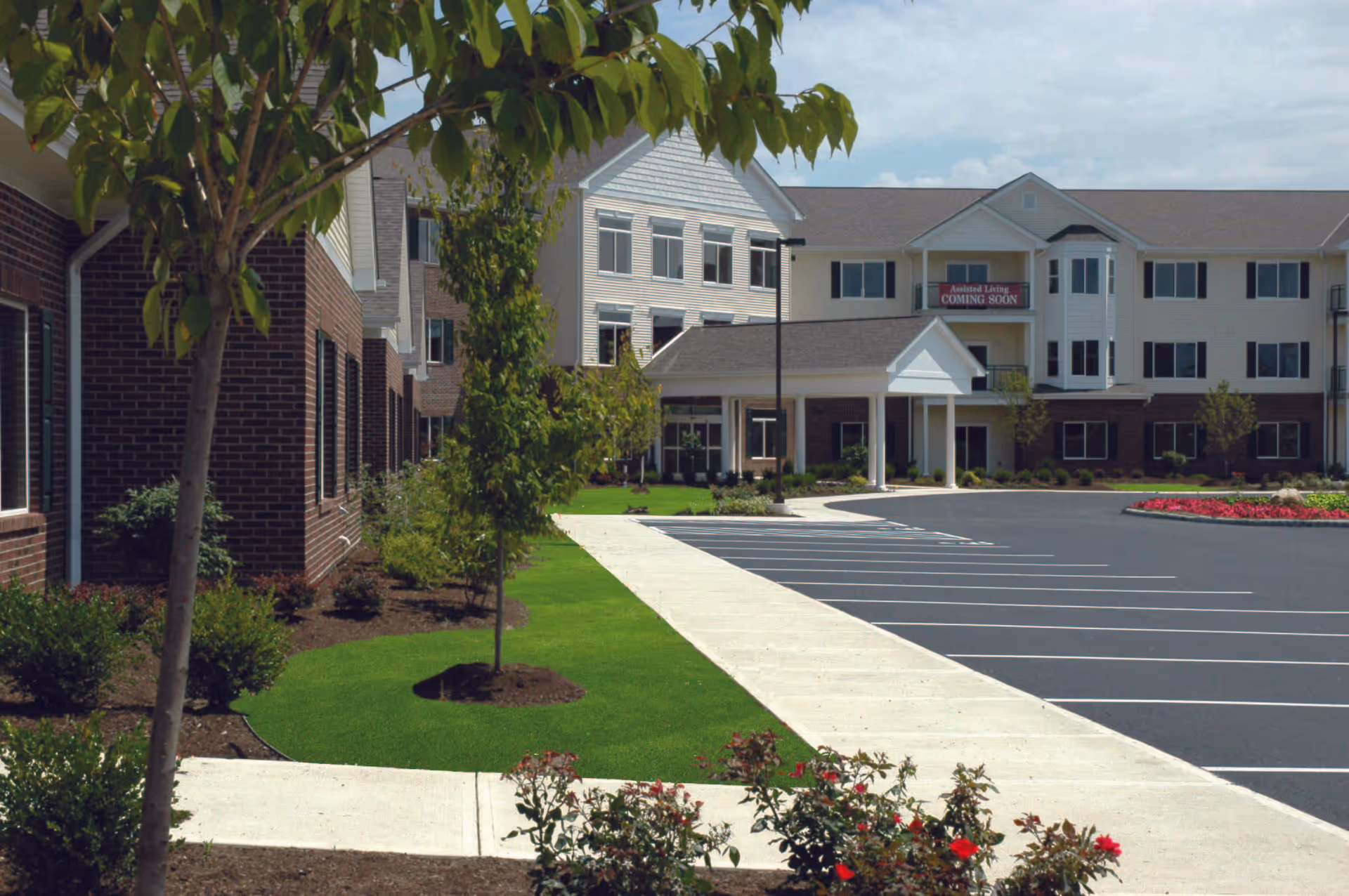 Front exterior of Willow Brook at Delaware Run senior living building with entrance, landscaped lawn, and empty parking lot.
