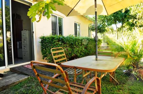Outdoor patio with table, chairs, an umbrella, and lush greenery beside the facility.