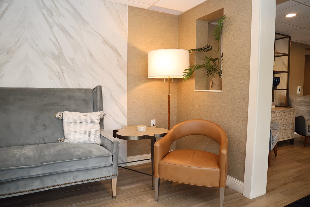 Cozy seating area with a gray loveseat, tan leather chair, round side table and floor lamp against a textured wall.