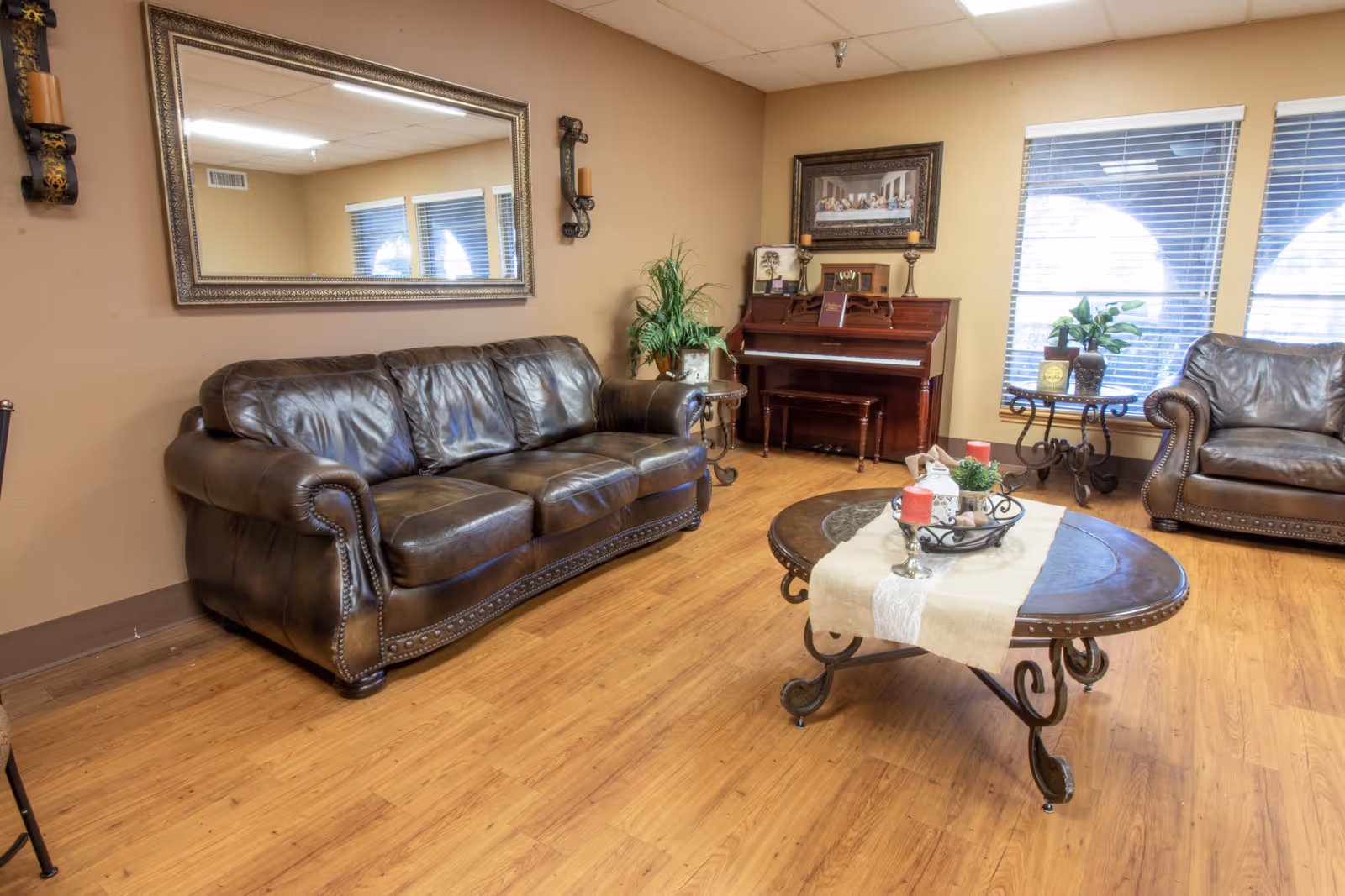 Comfortable seating area with leather sofas, a coffee table, a piano and decorative mirror in a warm, well-lit common room.