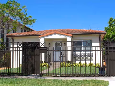 Small, single-story building with a metal fence, manicured lawn, and clear blue sky.