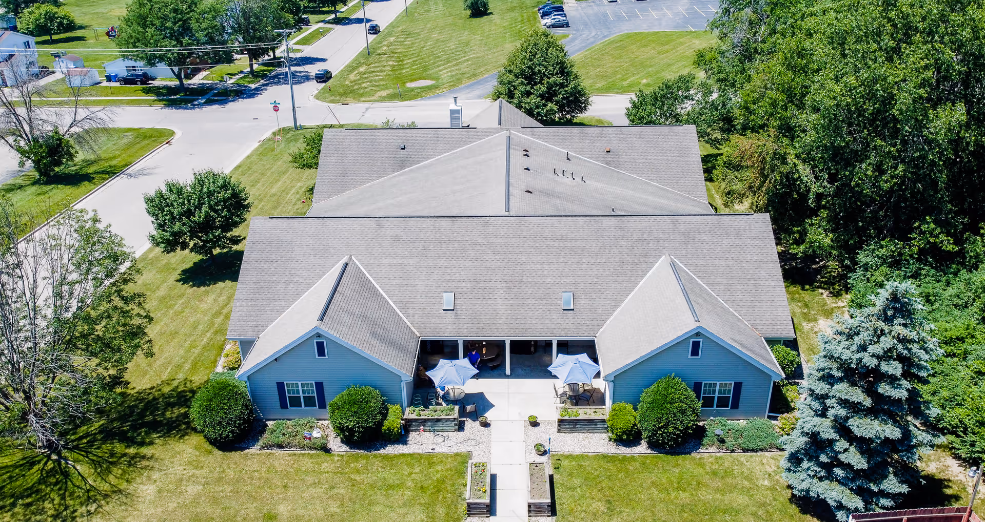 Aerial view of a single-story assisted living building with a central courtyard and patio umbrellas surrounded by lawns and trees.