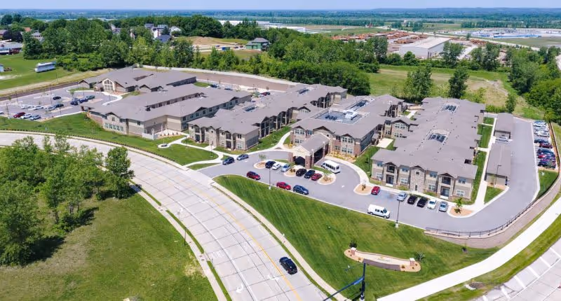 Aerial view of a large senior living facility complex with multiple connected buildings, parking areas, roads, and surrounding green space.
