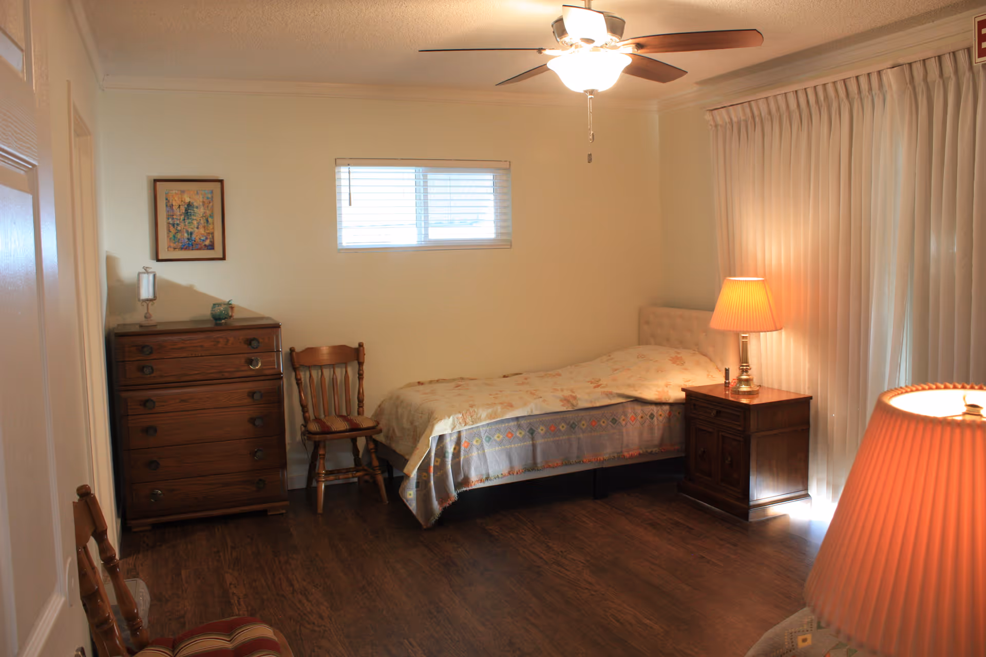 Senior living bedroom with a bed, dresser, nightstand, chair, and lamps.