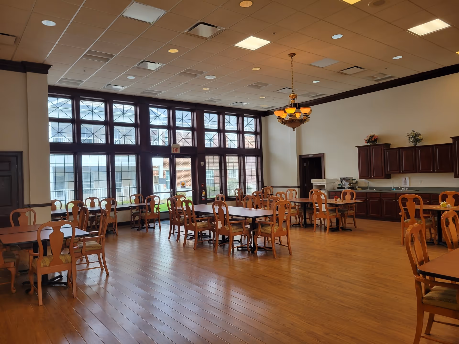 Spacious dining room with wooden tables and chairs, large multi-pane windows, and a serving counter with cabinets.