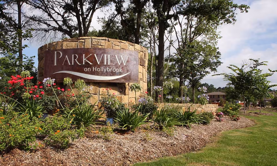 Stone sign for Parkview on Hollybrook surrounded by landscaped garden with various flowers and plants, trees in the background under a partly cloudy sky.